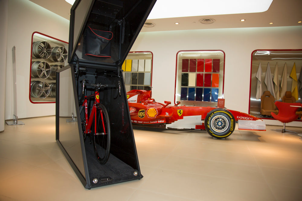 Bicycle inside a black Velohawk Storage Pod with a red Ferrari race car in the background